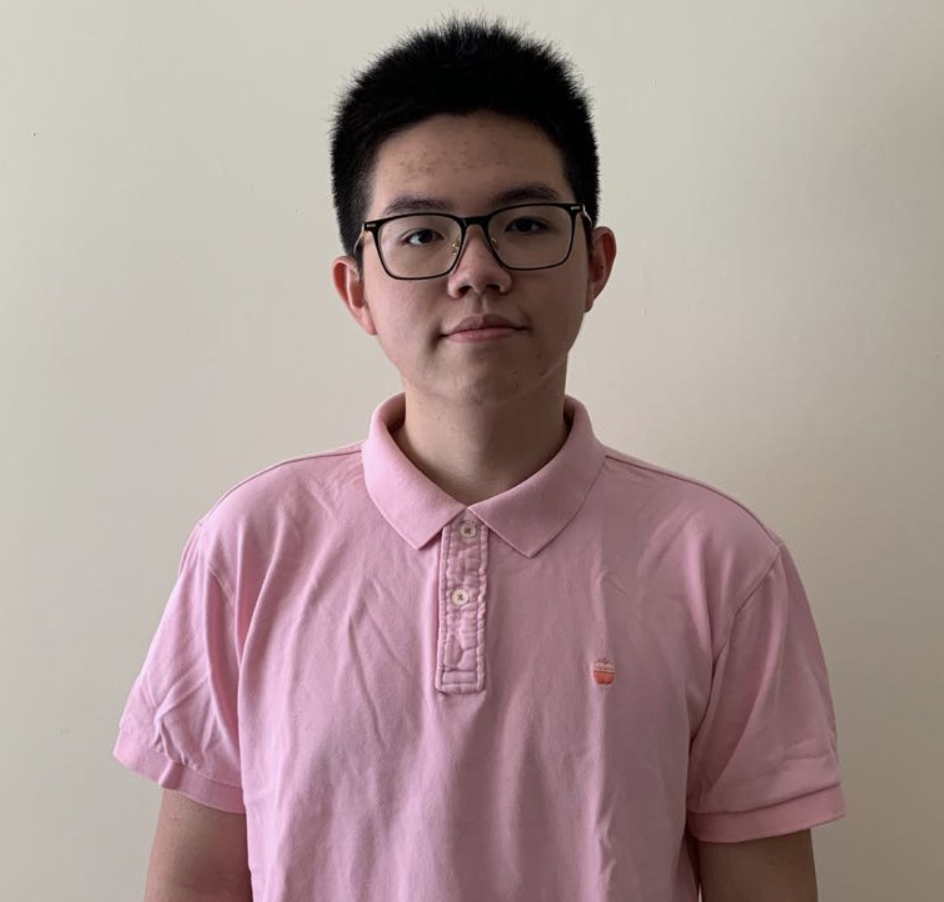 Portrait of young man with short black hair, glasses, and pink polo shirt.