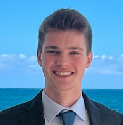 Young man in suit and tie smiling at view, ocean in background.