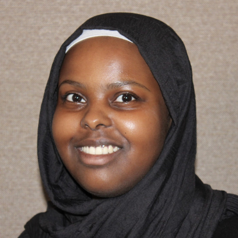 A young person wearing a black hijab smiles at the camera.