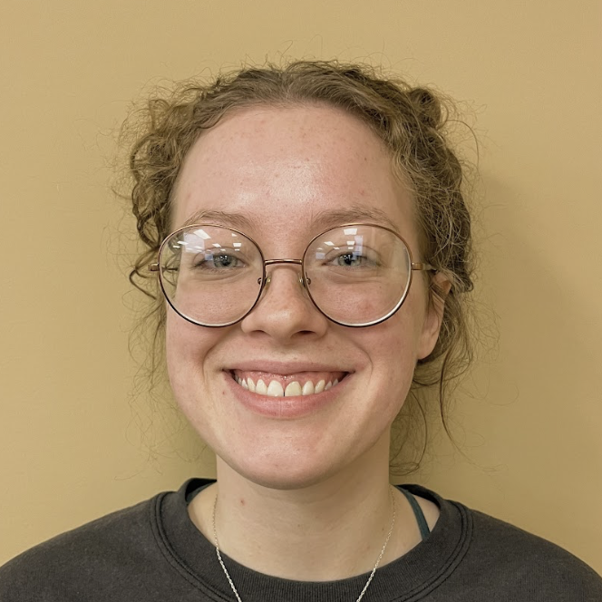 A young person in round glasses smiles at the camera. 
