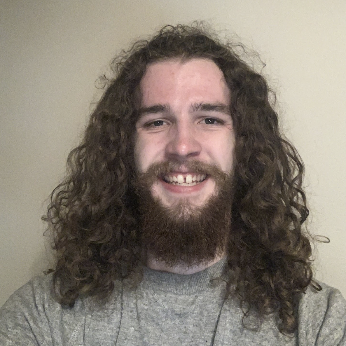 A young person with long curly hair smiles at the camera.