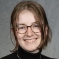 A young person with glasses wearing a turtleneck smiles.