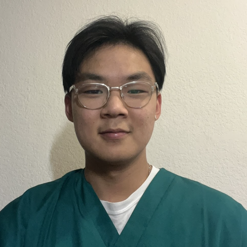 A young male-presenting person in teal scrubs smiles.