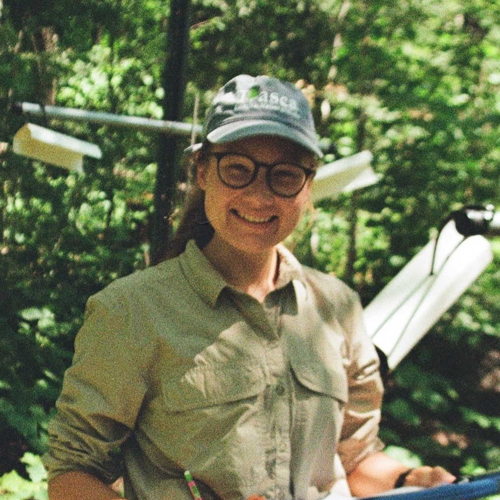 a young female-presenting person appearing to be doing fieldwork outside smiling.