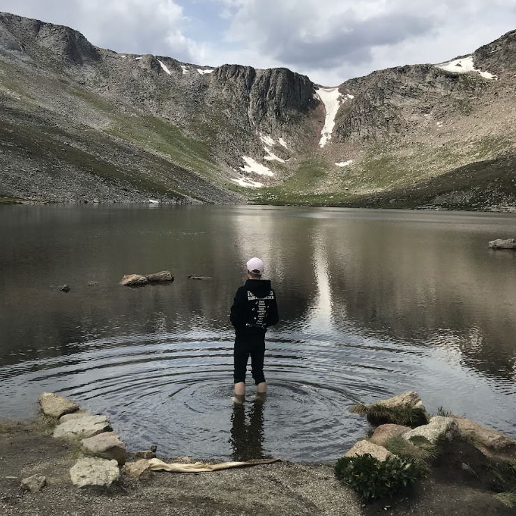 A person stands in a body of water and looks at mountains.
