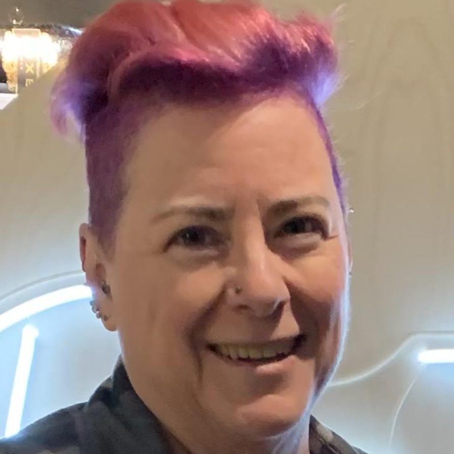 A person with pink hair smiles. 